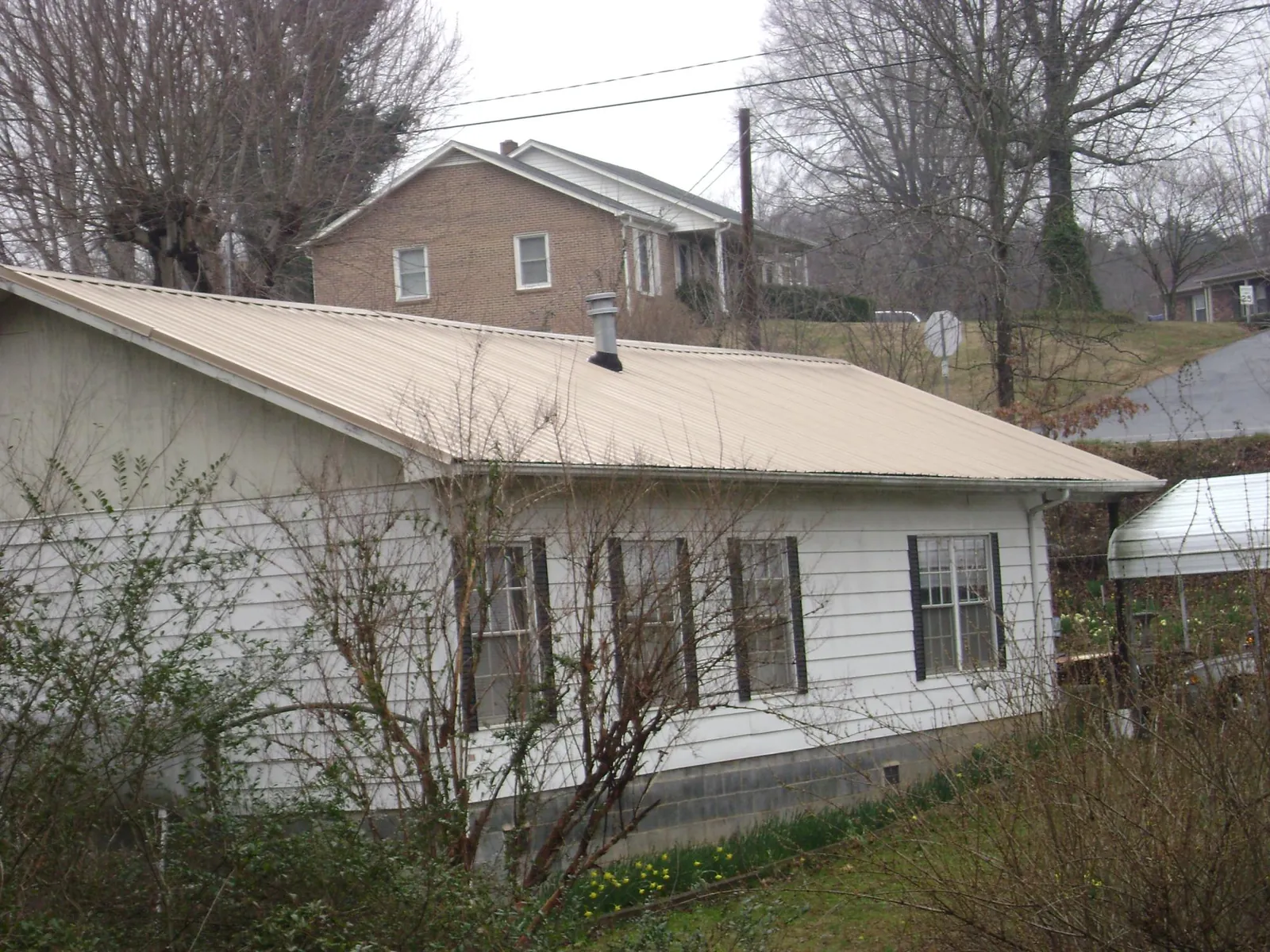 Tan metal roof on a white sided house set into a hillside — Commercial Roofing by Roofing Brothers in Chattanooga